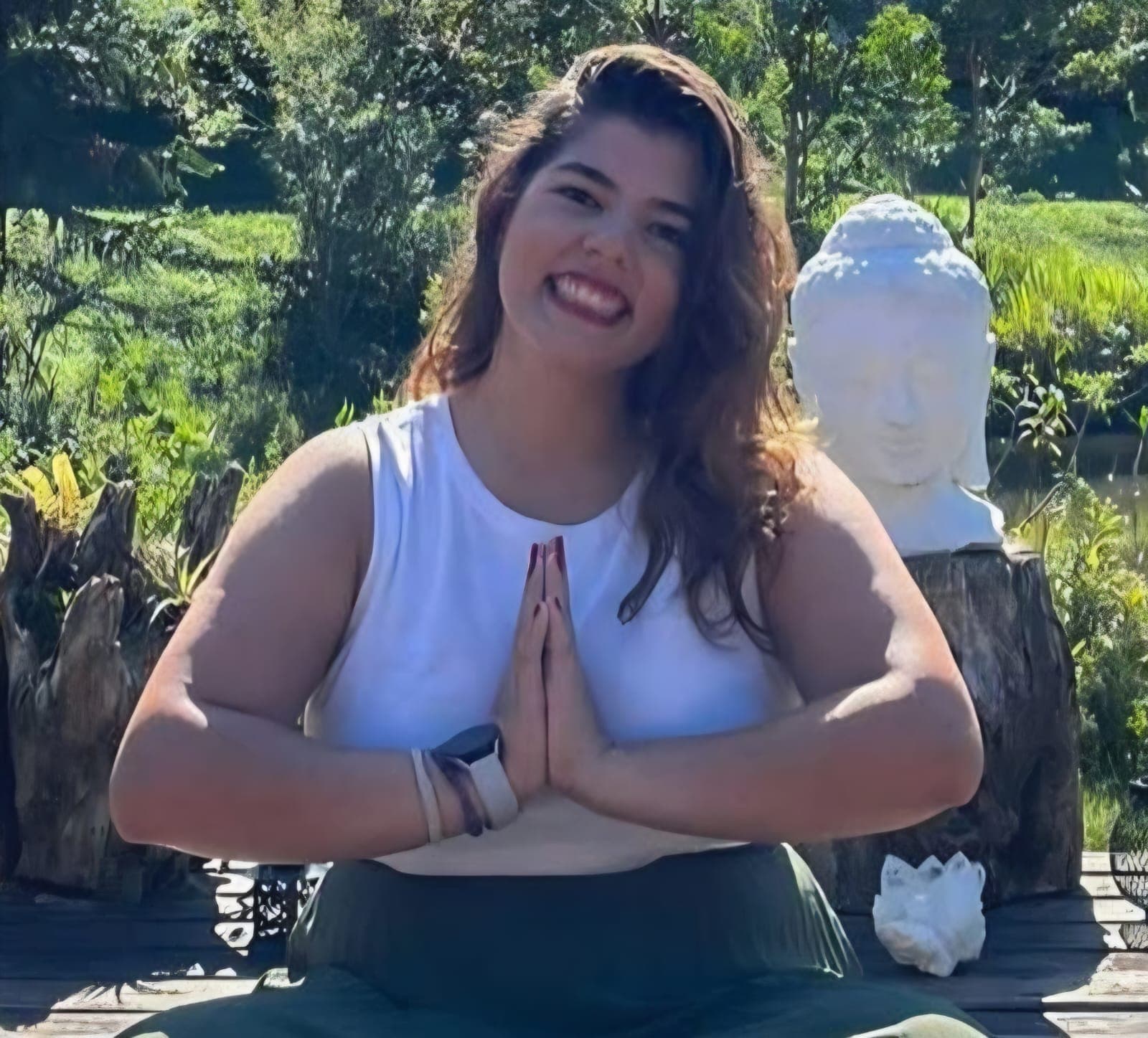 Isa Pupo de branco com as palmas das mãos unidas em ambiente arborizado.