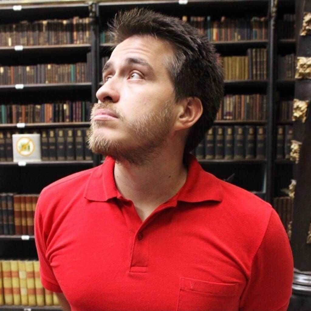 David em blusa vermelha, numa biblioteca repleta de livros.