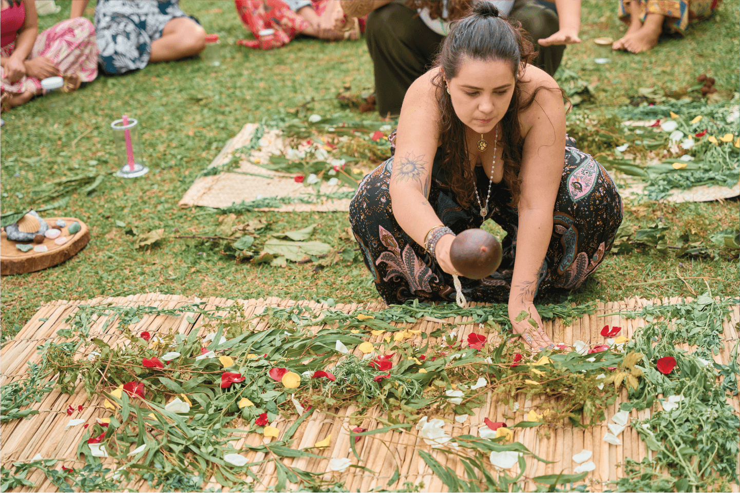 Ariane em um campo aberto com pessoas sentadas em circulo em volta enquanto ela organiza uma esteira de ervas.