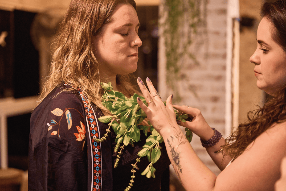Ariane aplicando ritual com ervas em uma mulher concentrada.