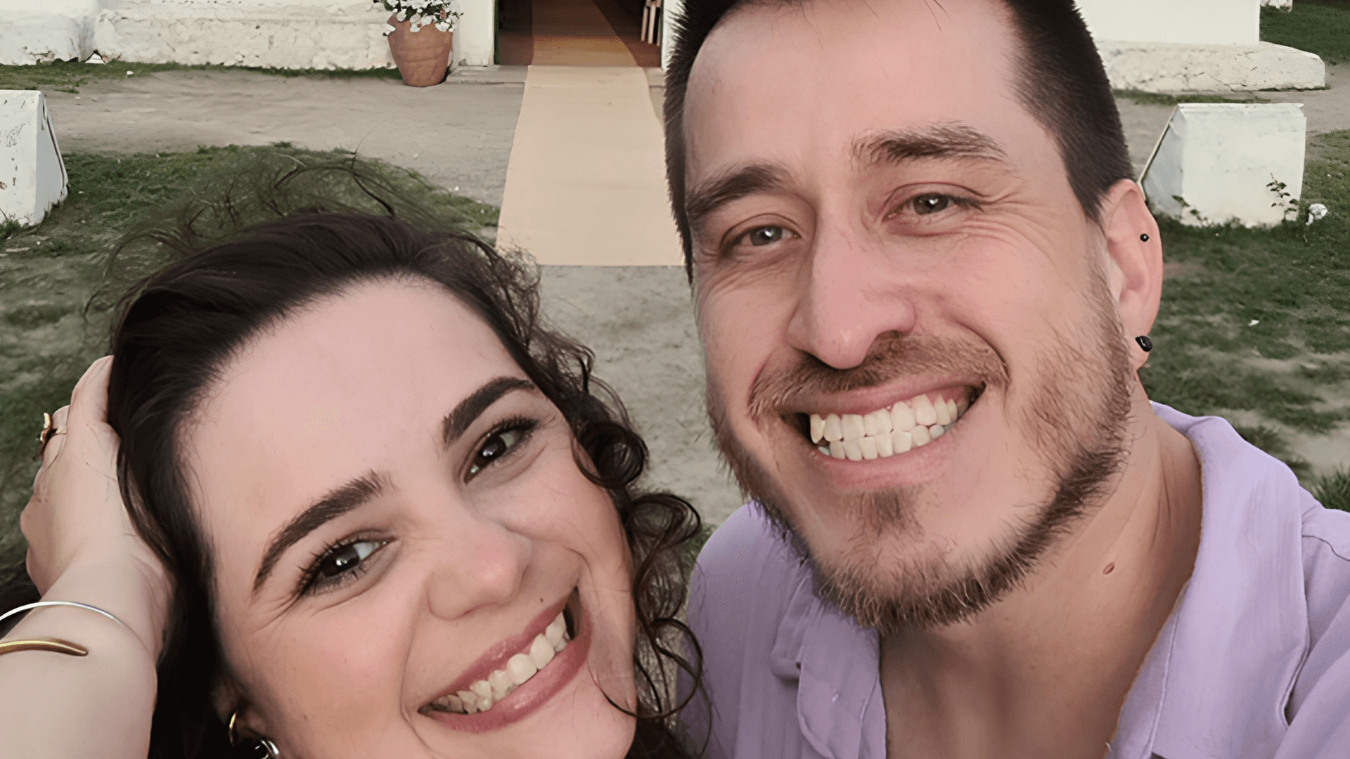 Ariane e David abraçados e felizes em frente a uma igreja.