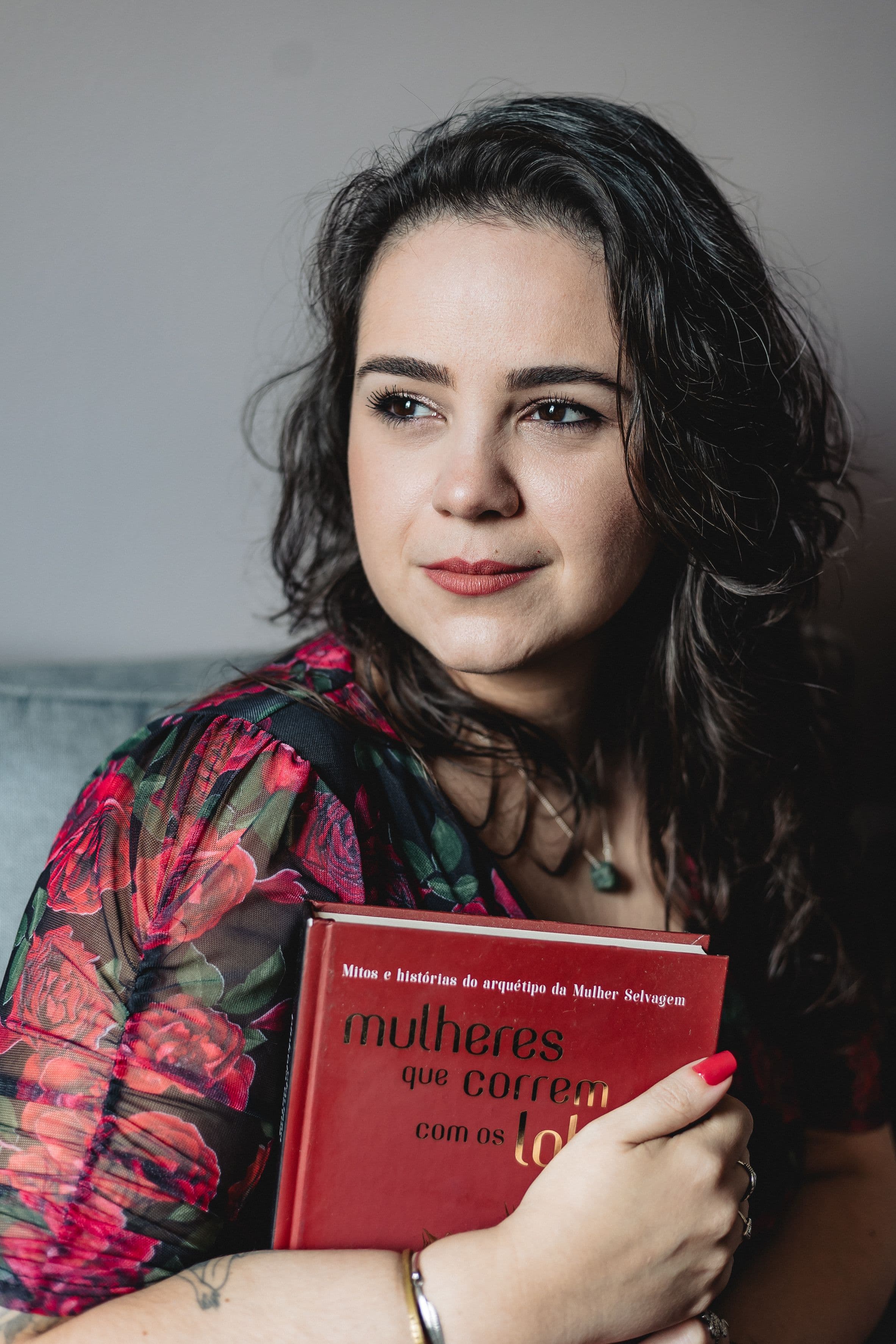 Ariane em vestido vermelho segurando o livro Mulheres que correm com lobos, também vermelho.