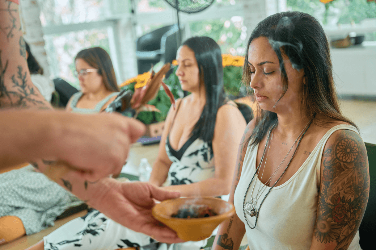 Mulheres sentadas no chão, concentradas enquanto acontece ritual com incensos.