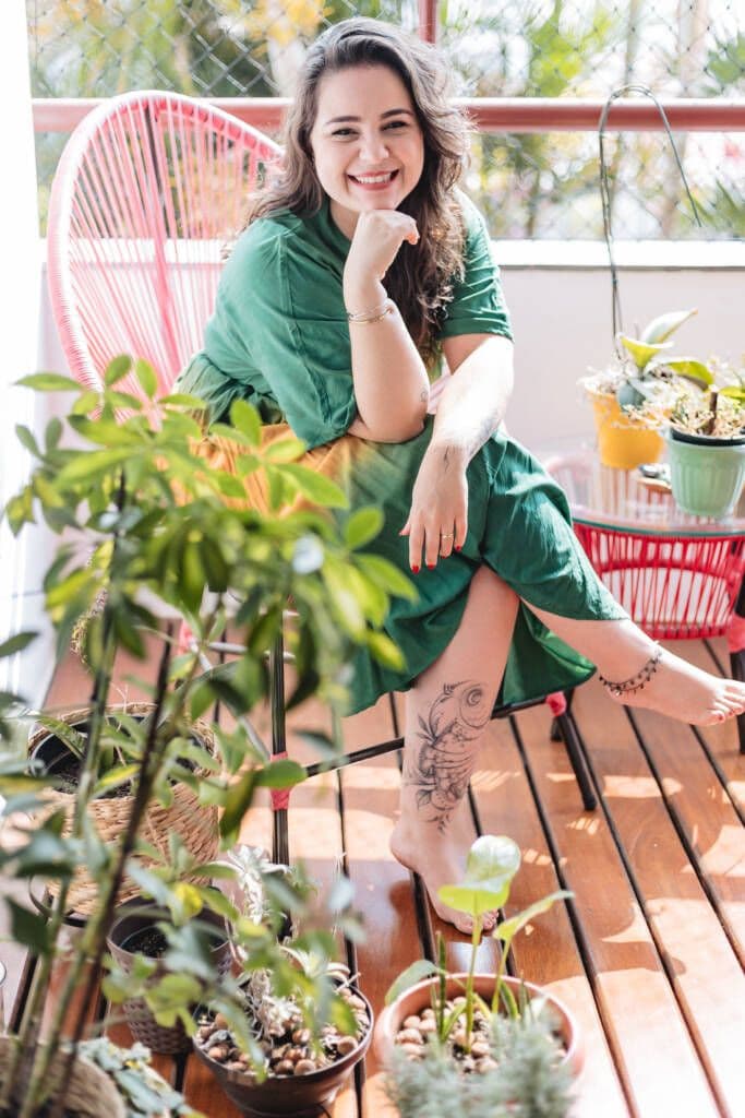 Ariane de verde sentada em uma cadeira, feliz em ambiente arborizado.